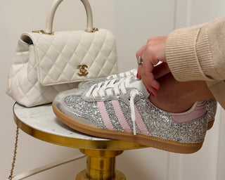 Silver glittery sneaker with pink stripes on a small round table, next to a white quilted handbag.